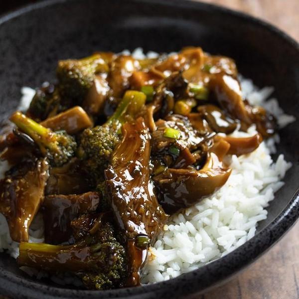 Teriyaki mushrooms and broccoli on white rice in a black bowl 