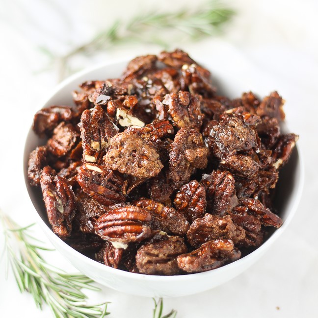 candied pecans in a white bowl next to rosemary