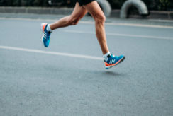 A runner, pictured from the legs down, runs along a road. They are wearing brightly coloured trainers. 