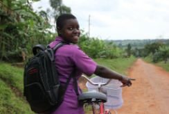 Nawalat, dressed in a purple school uniform, looks over her shoulder. She stands with her bicycle, about to embark on her journey to school.