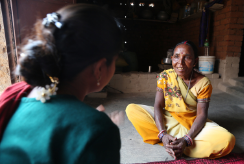 Two women are pictured in conversation. One has her back to the camera. The other, in a yellow Sari, looks towards her.