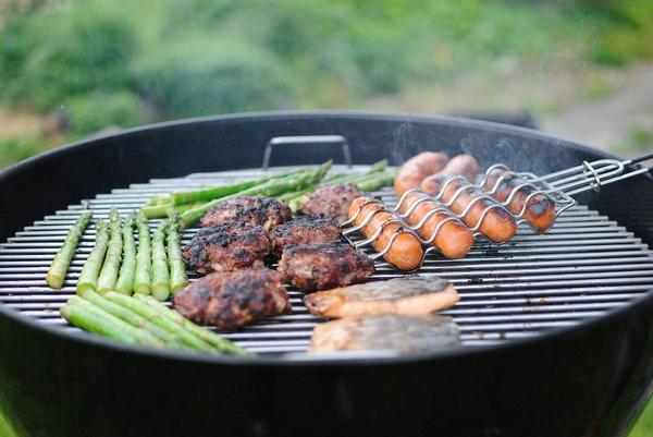 Close up of a charcoal grill with vegetables, burgers, and hot dogs