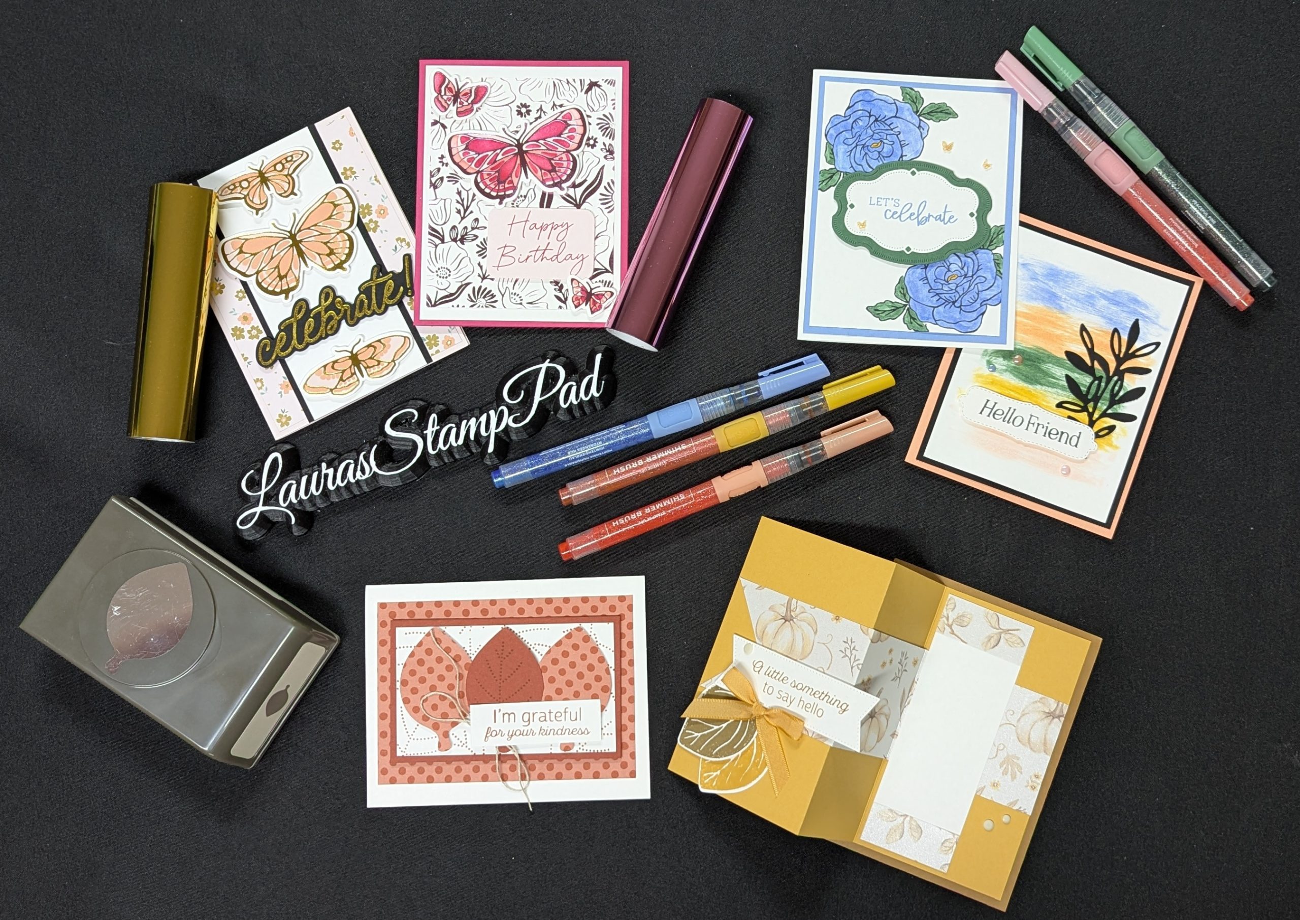 A colorful flat-lay of handmade fun-fold greeting cards in rose, sage and coral cardstock surrounded by crafting tools