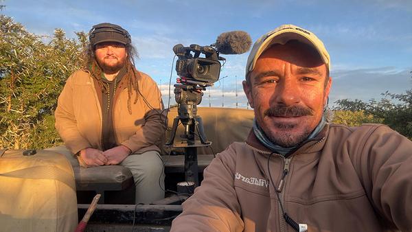 Two men in a safari vehicle with film equipment