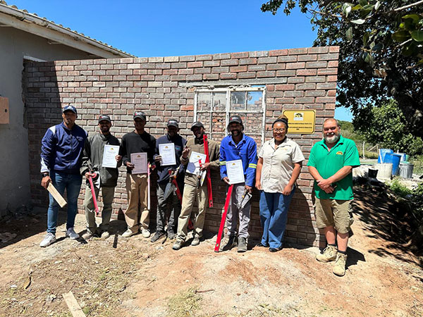 Community members standing in front of wall displaying their certificates