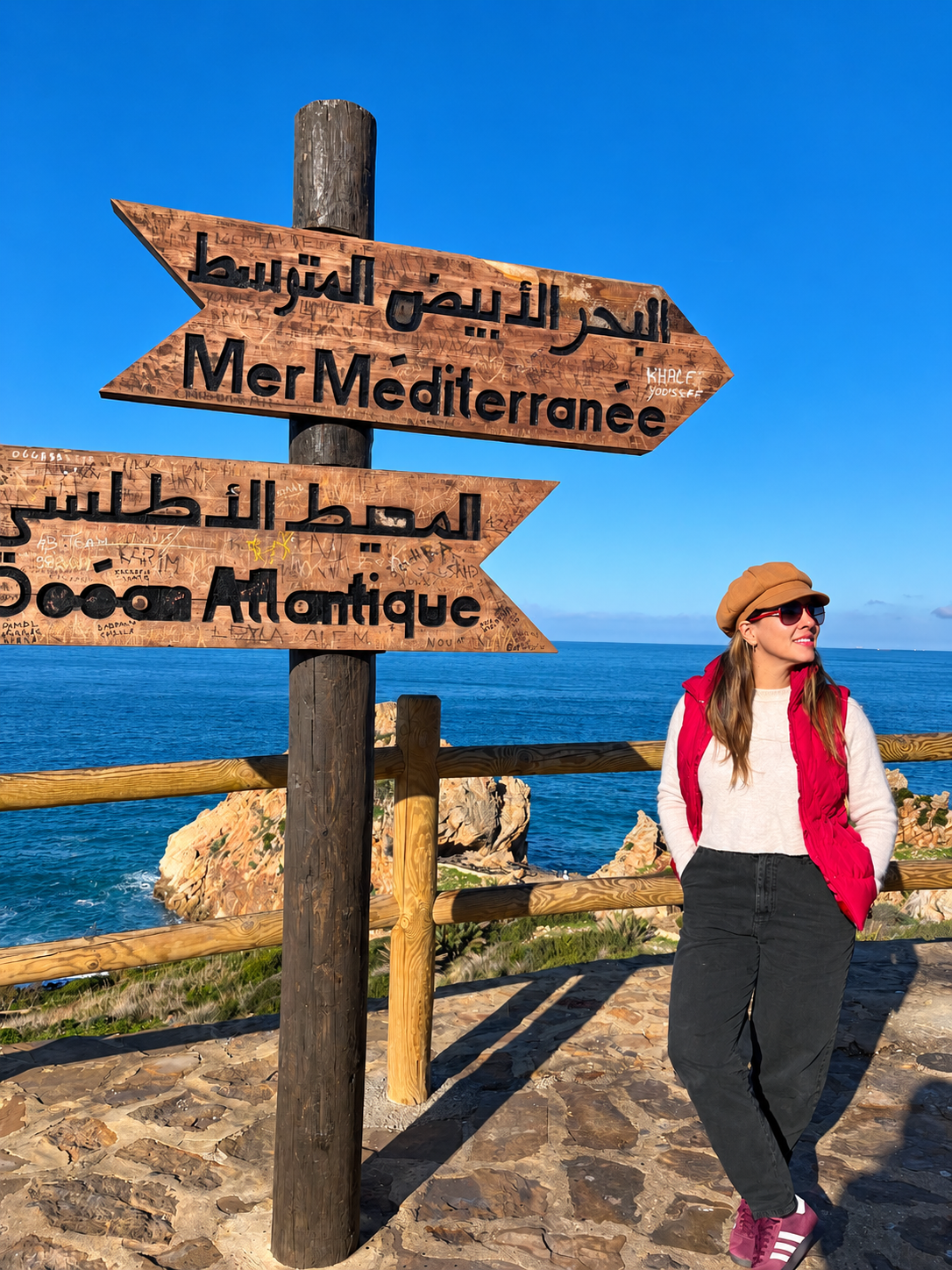 Claudia Velásquez de viaje, junto al mar, ante señales de dirección hacia el Mediterráneo y el Atlántico