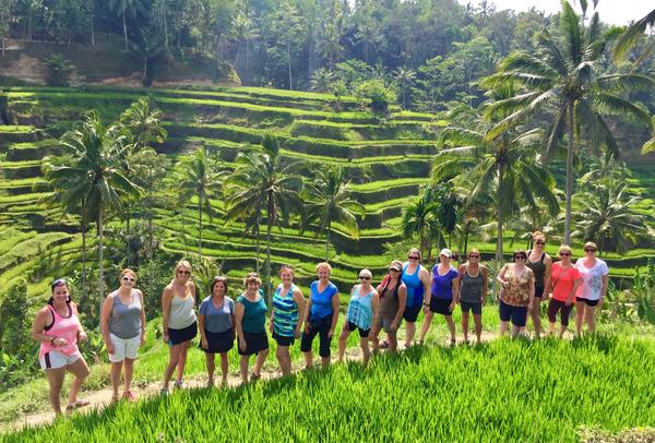 Group of smiling women stand in a line with Bali rice terraces behind them.