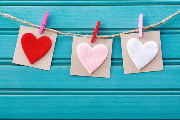 Three felt hearts attached to a piece of twine by clothespins and hanging over a turquoise shiplap wall 