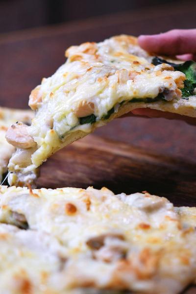 closeup of holding a slice of spinach alfredo pizza
