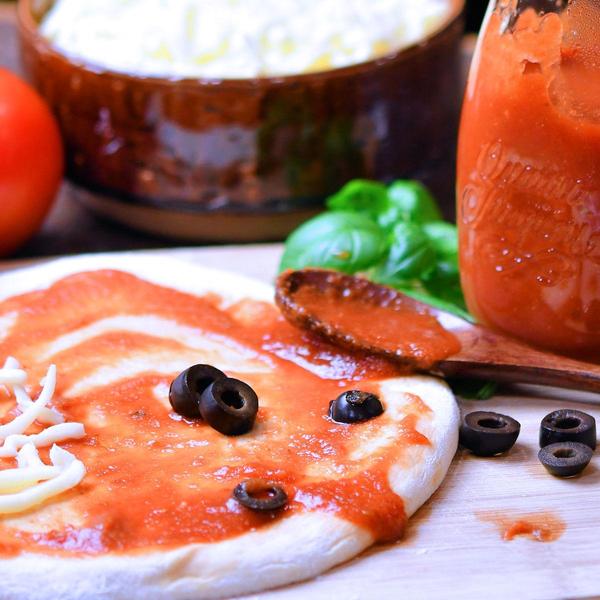 pizza dough rolled out on a cutting board with homemade sauce