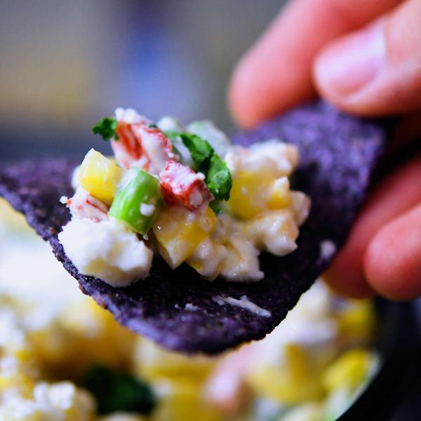 Scoop of Mexican corn dip on a blue tortilla chip