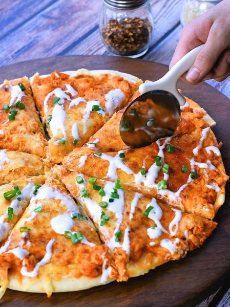 buffalo chicken pizza with pizza cutter on cutting board