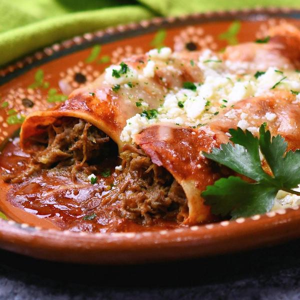 two beef enchiladas on a red clay oval plate