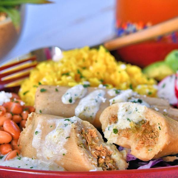 closeup of chicken tamales cut in half with beans and rice on the side
