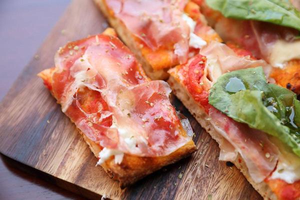 slices of prosciutto provolone pizza on a cutting board