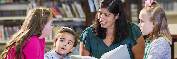 A teacher reading in the library with three students