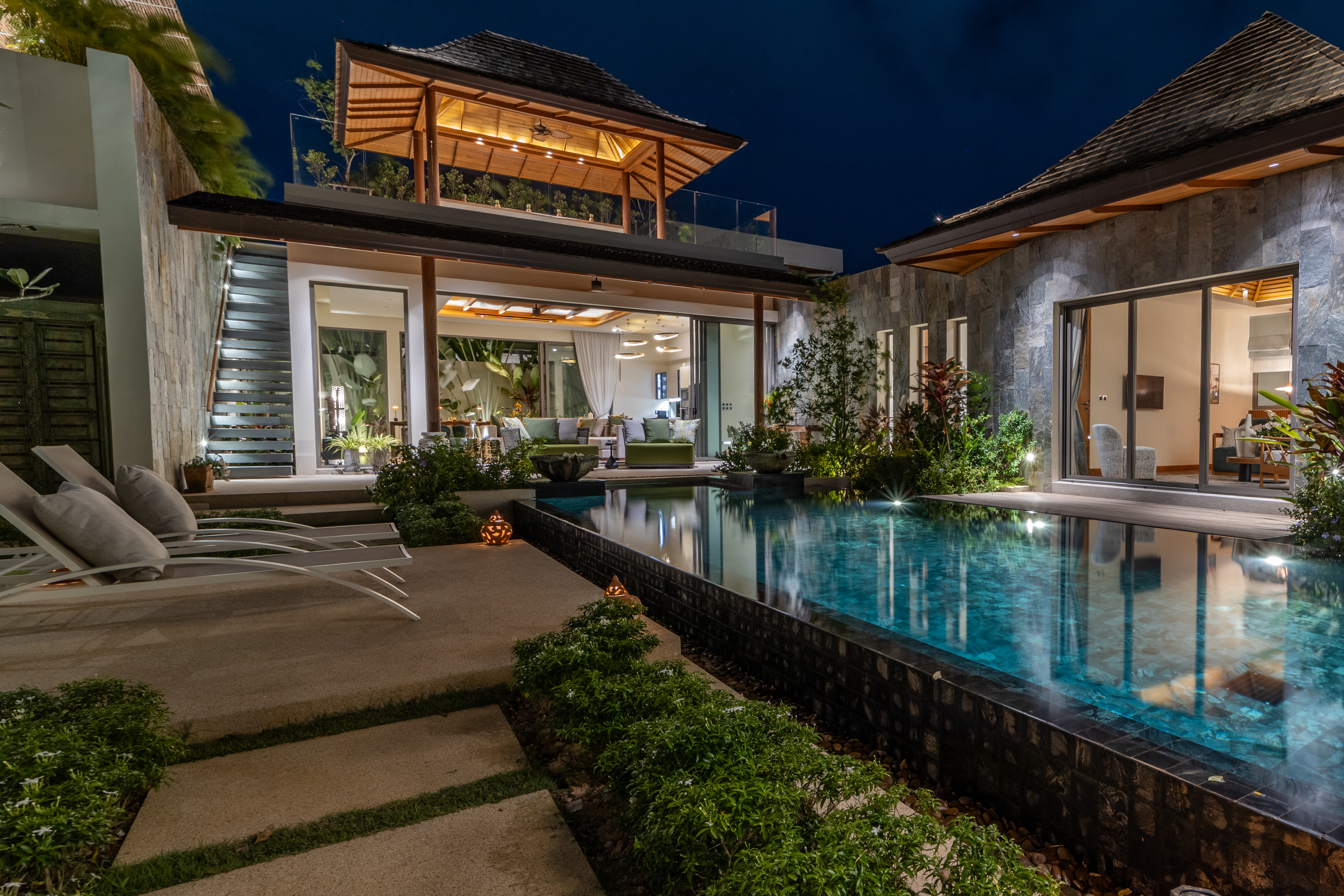 Luxury Phuket pool villa lit up at night, with a Thai-style sala on the roof terrace and a glowing infinity pool