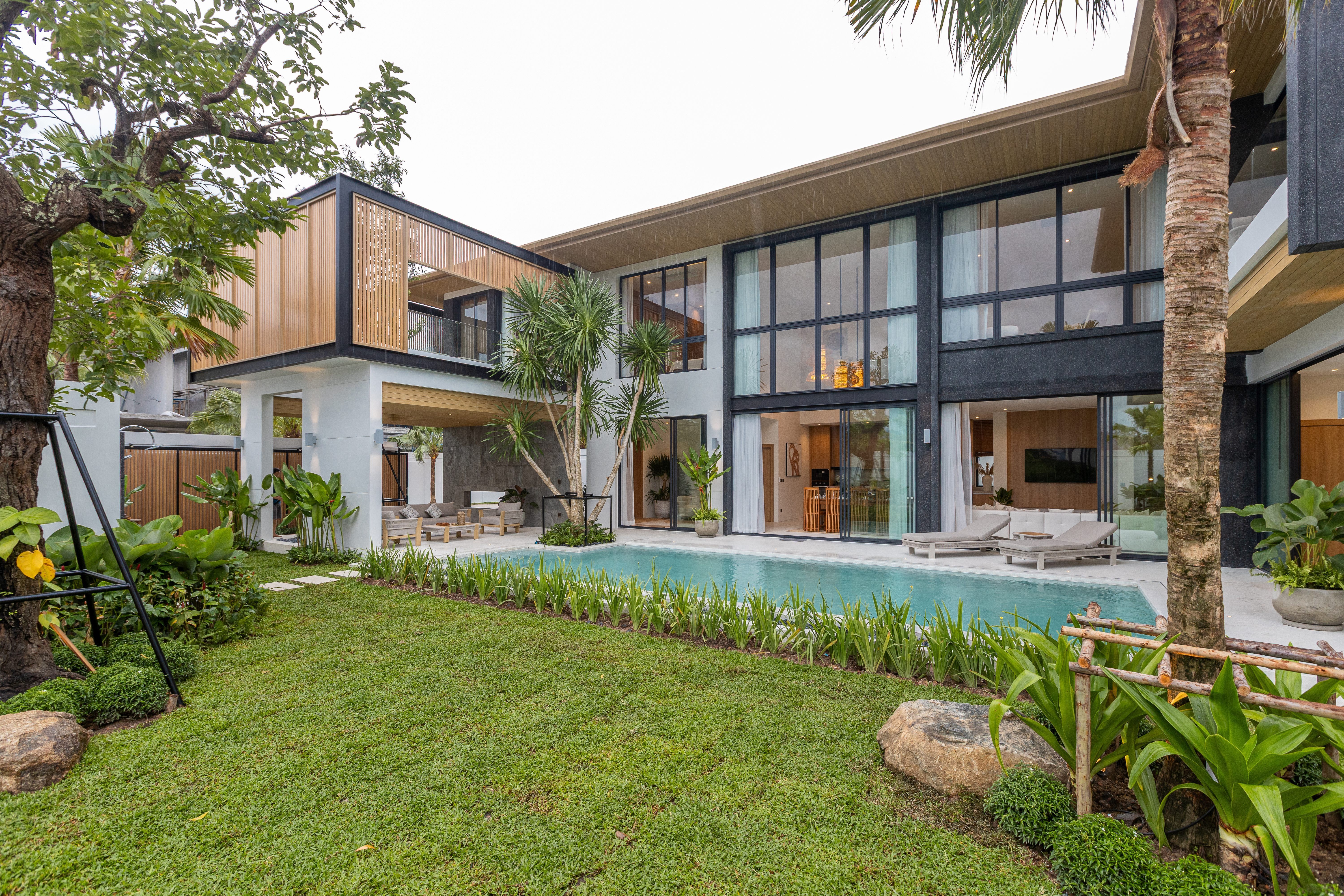 Contemporary two-storey Phuket pool villa with timber screens, floor-to-ceiling glass and a tropical garden