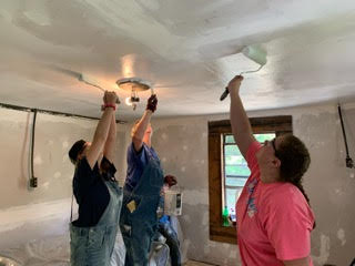 Christie (middle) working with her team painting ceiling and walls of a home after they mudded and sanded it.