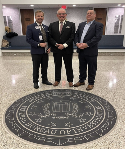 Chris, Jaime and Mathew standing behind the plaque in floor at FBI