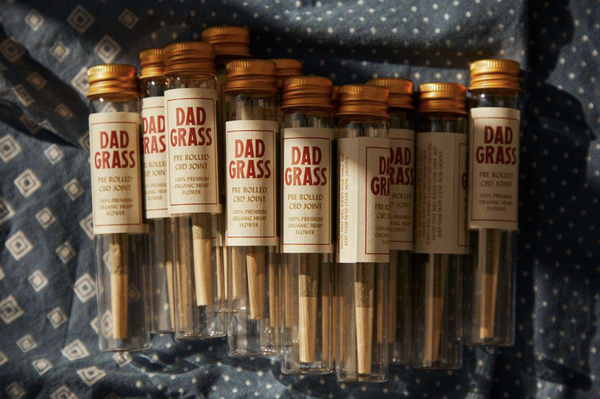 Custom pre-rolled CBD joints from our friends at Dad Grass rolled up in cute little bottles on a blue tablecloth