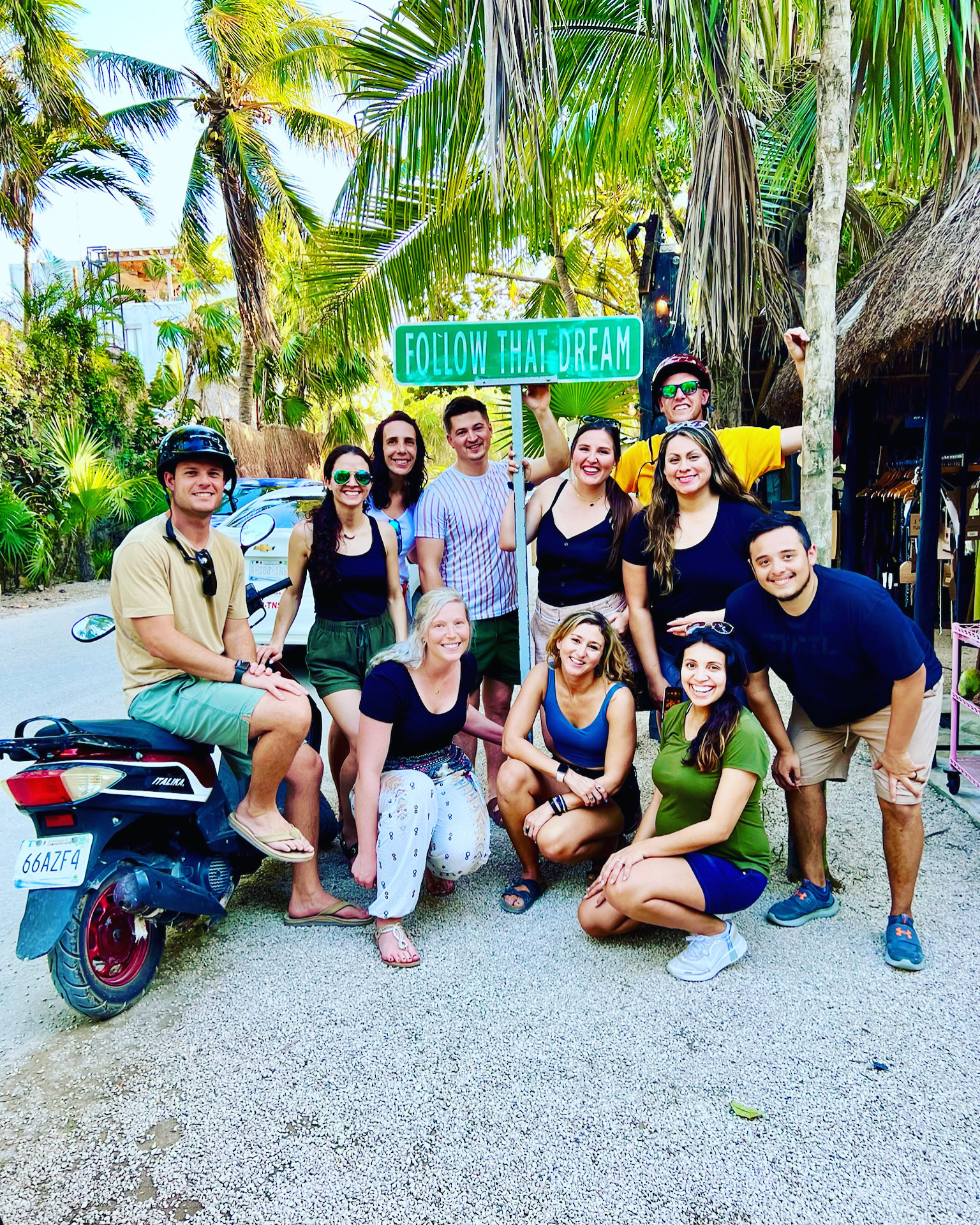 A happy group of friends gathered under a FOLLOW THAT DREAM street sign in Tulum
