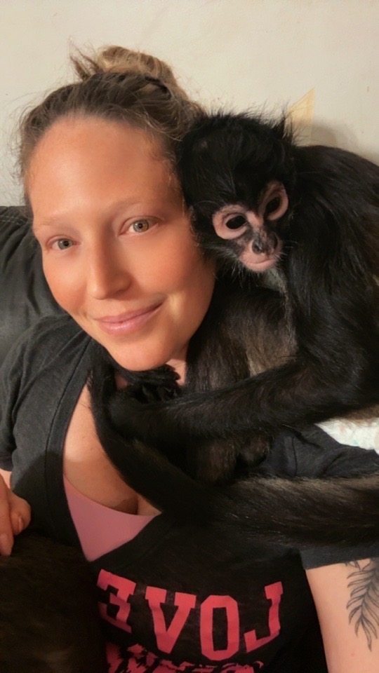 Myrah smiling with a spider monkey resting on her shoulder