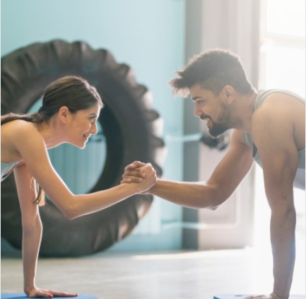Two people working out together and grasping hands in the plank position.