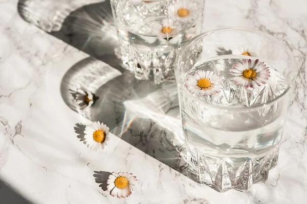 Glass of clear water and daisies next to glass