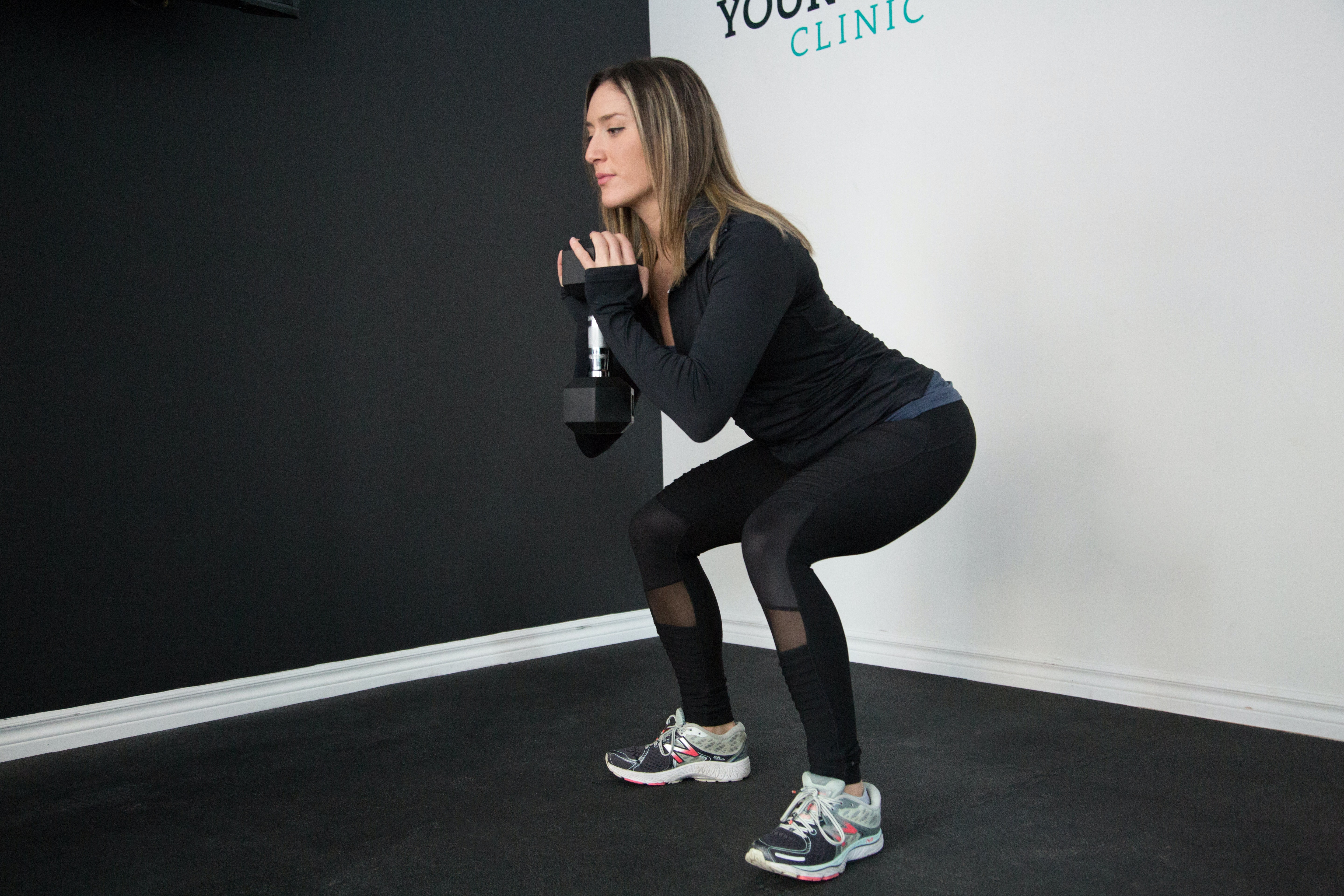 Woman doing a partial squat while holding a light dumbell