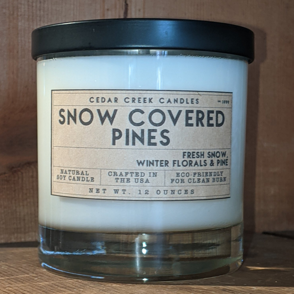 Image of a snow covered pines scented candle from the Cedar Creek Candles on a table.