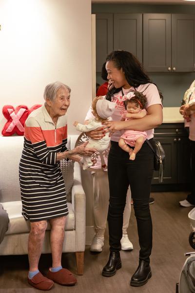 A DreamShyre team member handing a baby doll to a delighted senior woman