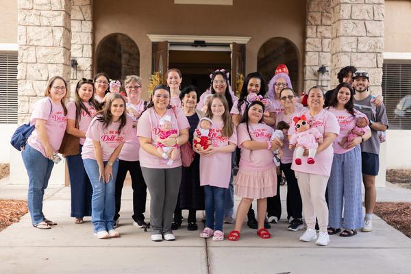 The DreamShyre team, volunteers and residents in matching pink Be My Doll-entine shirts, holding baby dolls outside a senior home