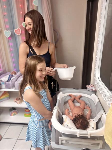 A mother and daughter smiling while giving a baby doll a bath in the nursery