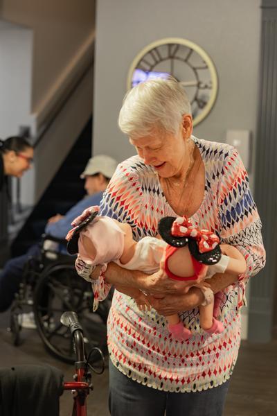 A senior woman laughing as she rocks a baby doll wearing Minnie Mouse ears