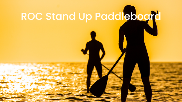 silhouettes of a man in the distance and a woman in the foreground paddleboarding against a golden sky during sunset.