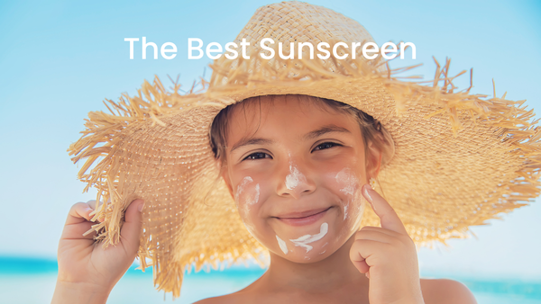 child with a sunhat on smearing white sunscreen on his face with an aqua blue sea and sky behind him.