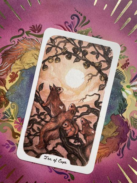 Ten of Cups tarot card by Oak, Ash & Thorn. 4 squirrels admiring the sun and sky under 10 acorn cups on a branch