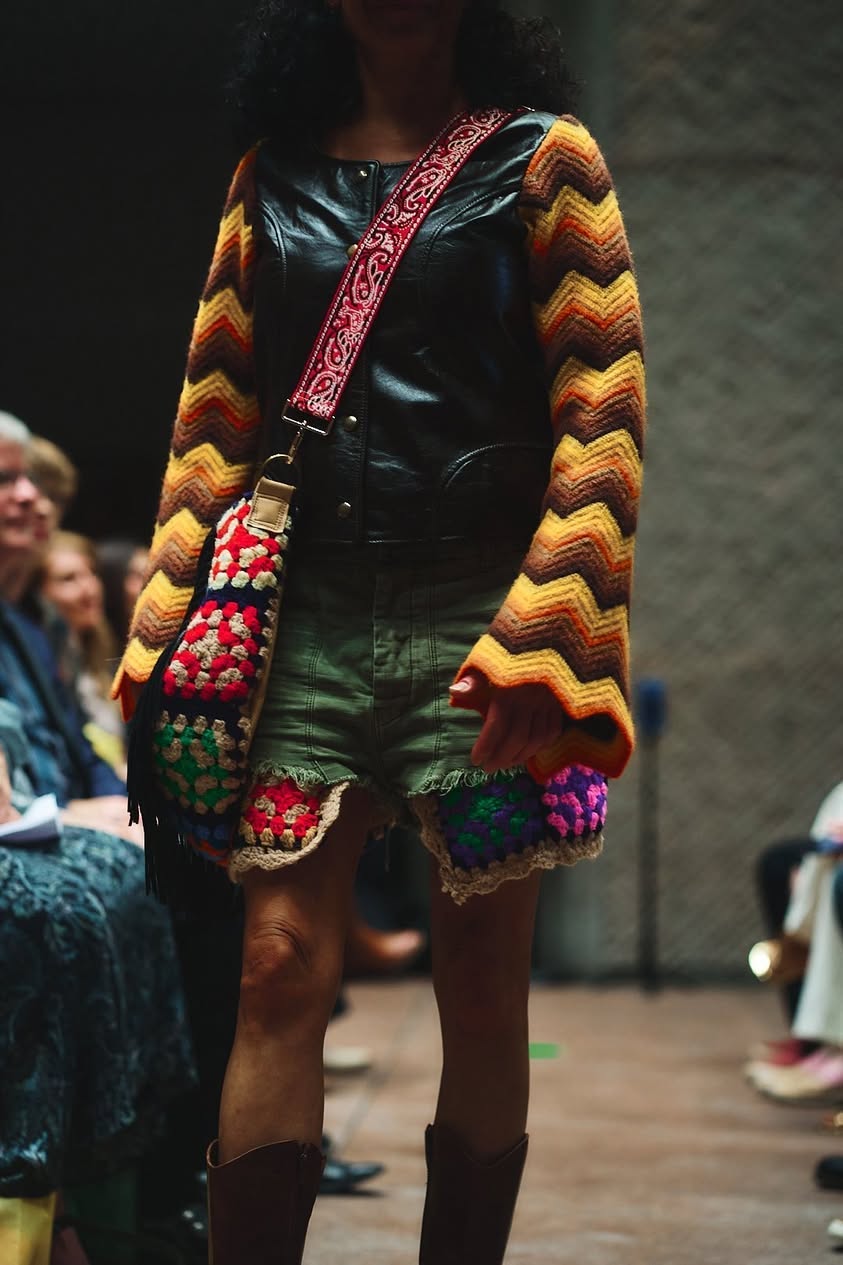 Runway look pairing a leather jacket with zigzag crochet sleeves, granny-square bag, and distressed denim shorts