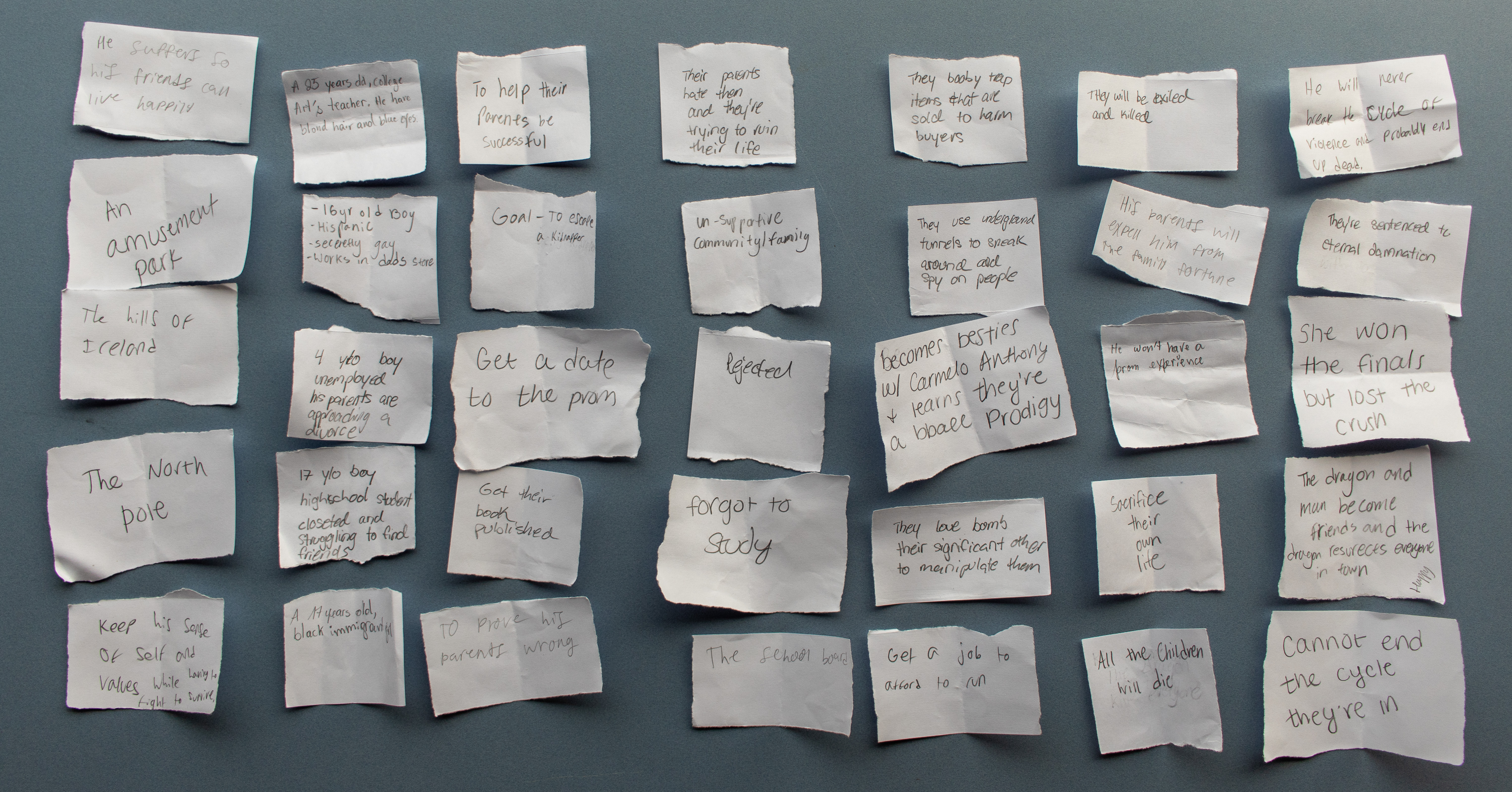Dozens of handwritten story-idea cards — characters, goals, and settings — laid out across a table