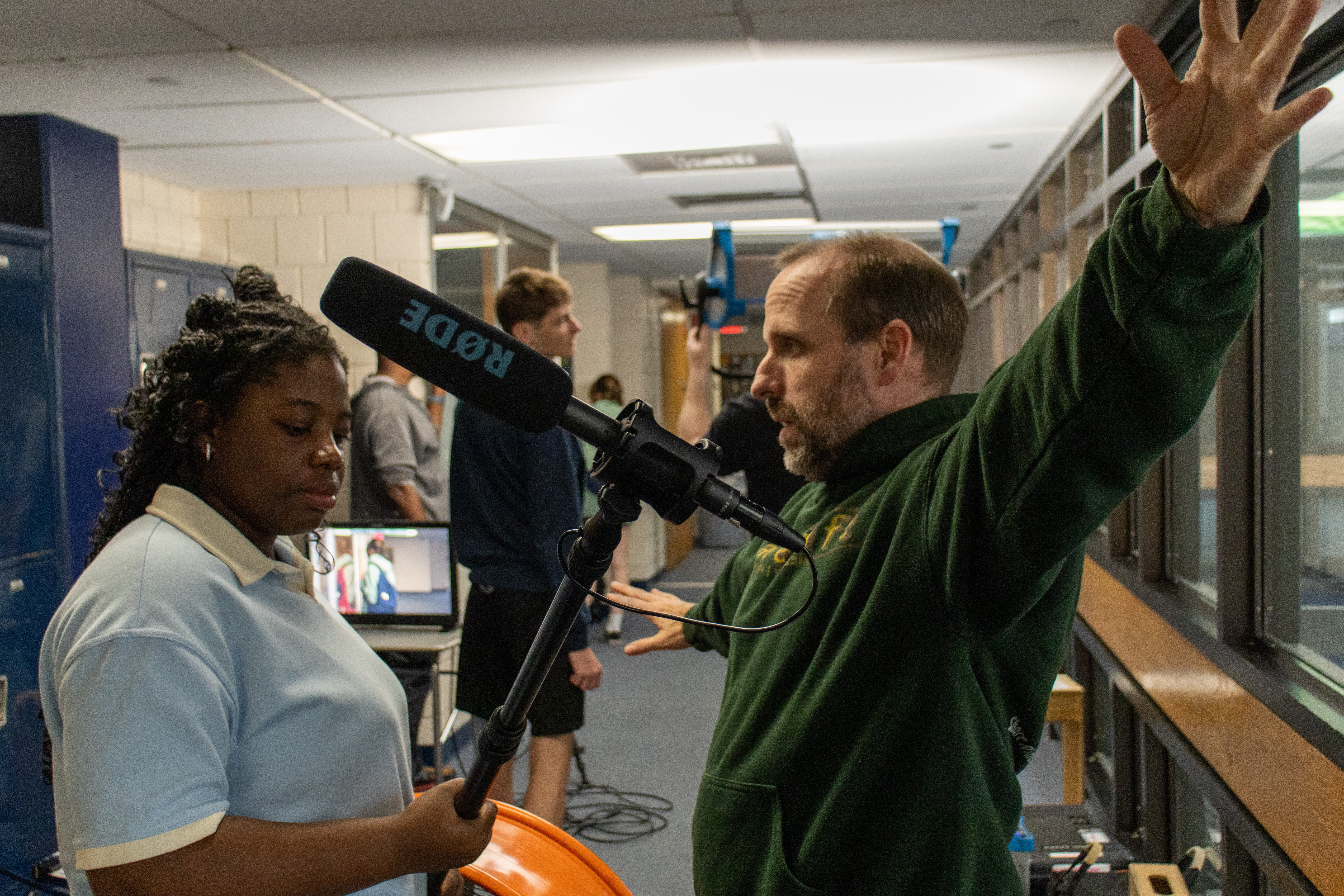 An instructor directs a student holding a boom mic in the hallway on set