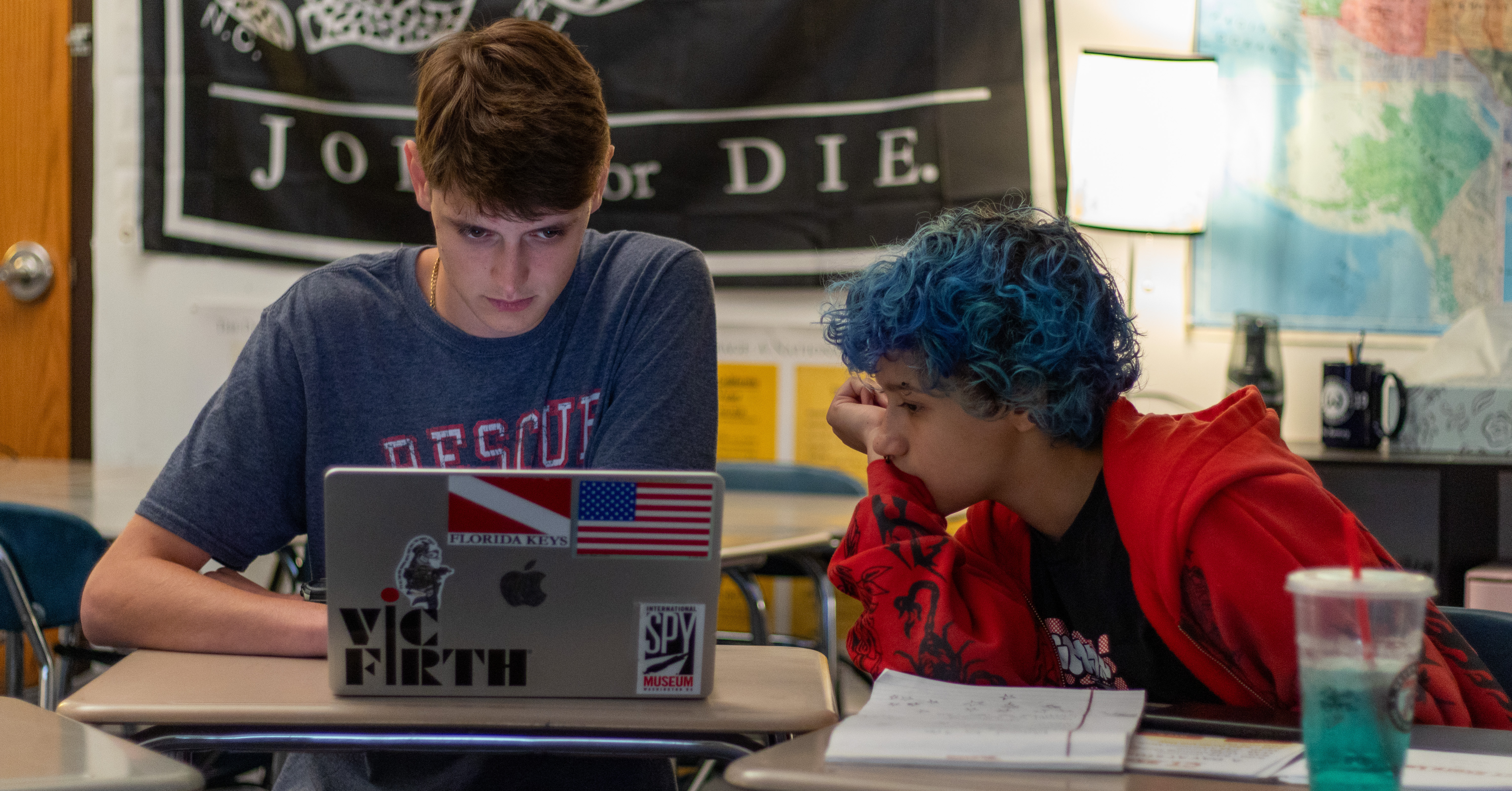 Two teen writers working closely together at a laptop, heads down and focused