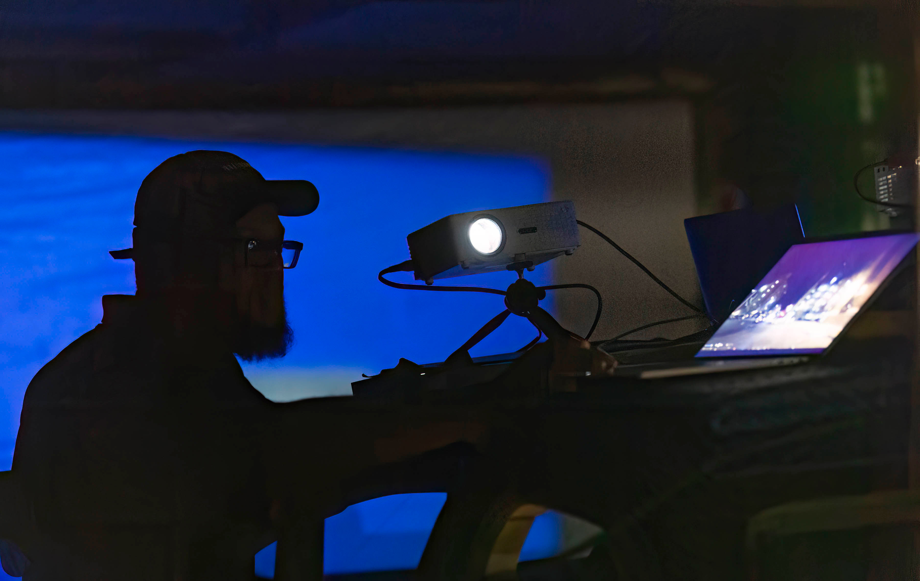A crew member silhouetted at a projector against a glowing blue screen on set