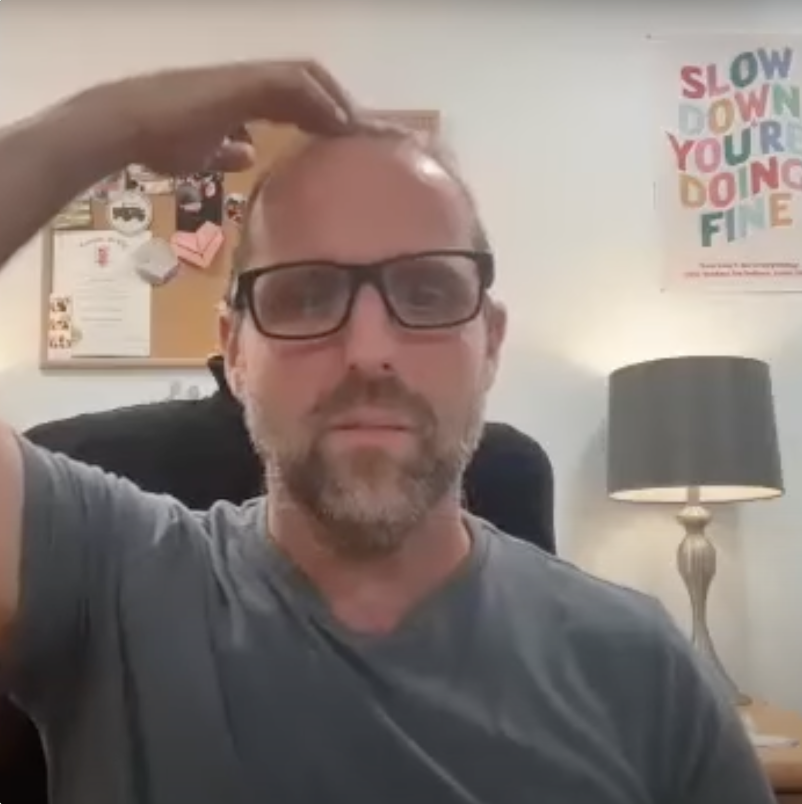 Brian Hogan at his desk, a playful moment beneath a colorful ‘Slow Down, You’re Doing Fine’ poster