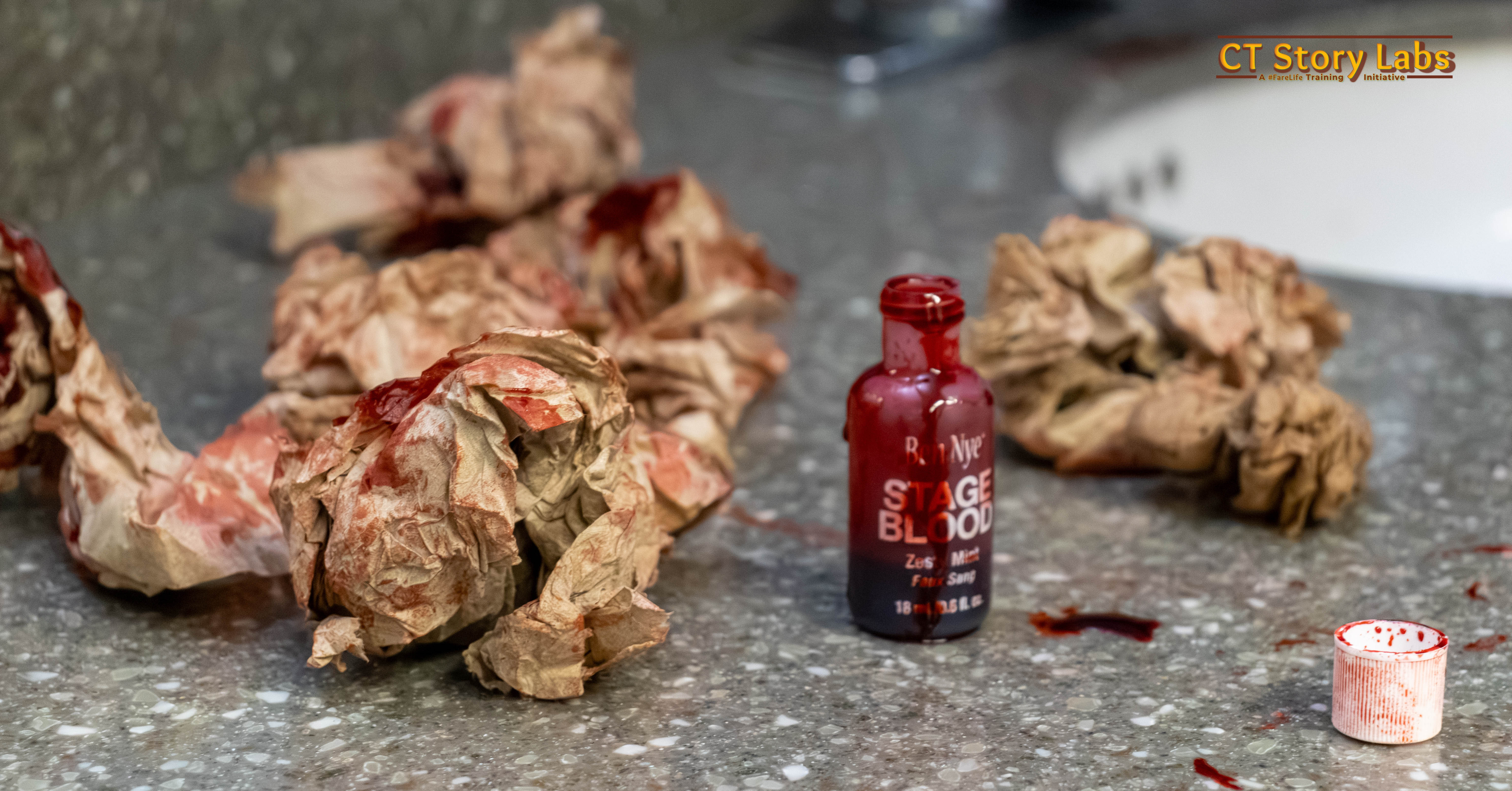 A bottle of stage blood and blood-dabbed prop paper on a countertop