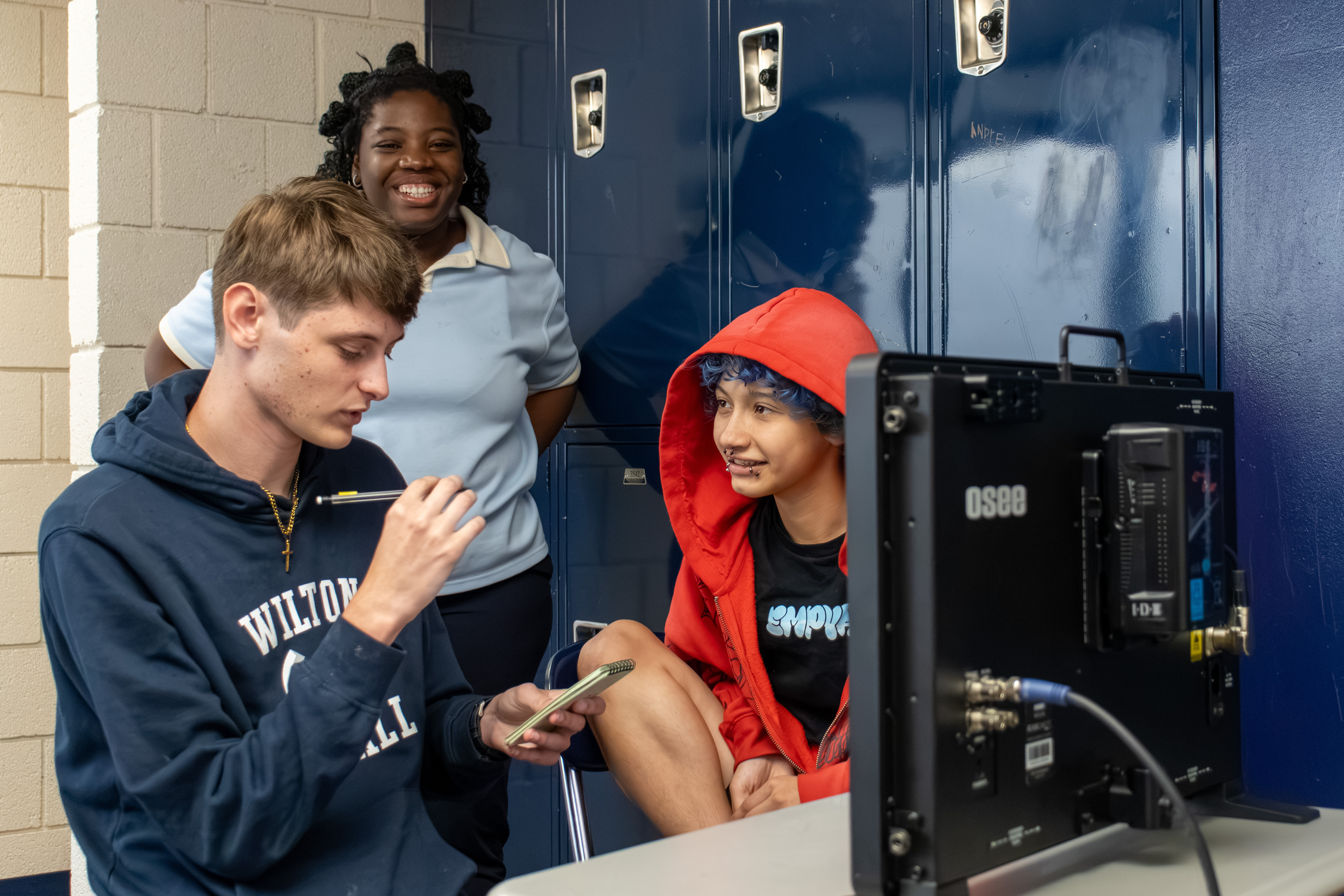 An instructor and two students smile at a monitor while reviewing a shot together on set