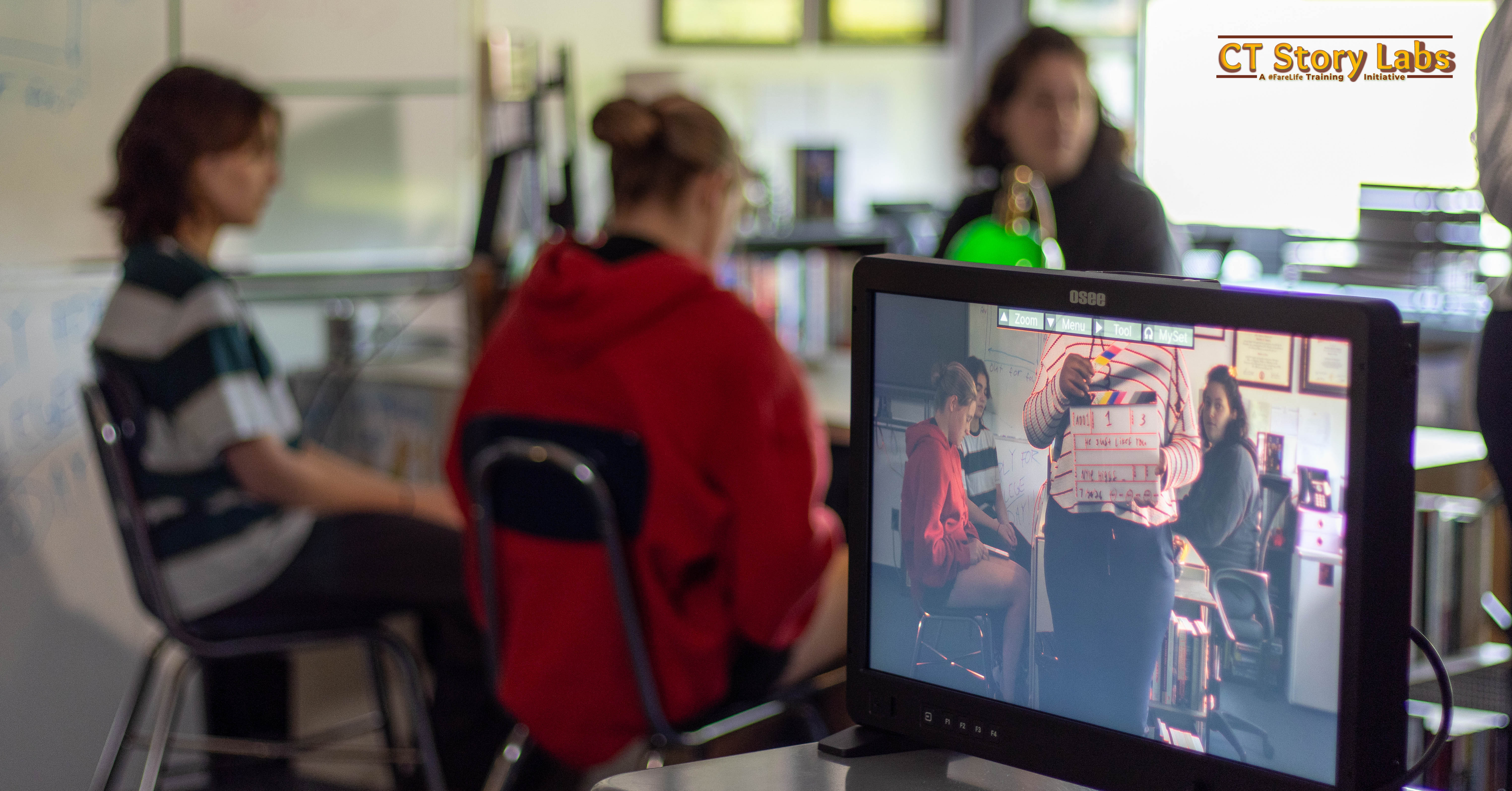 A director's monitor showing a scene being filmed while the crew works