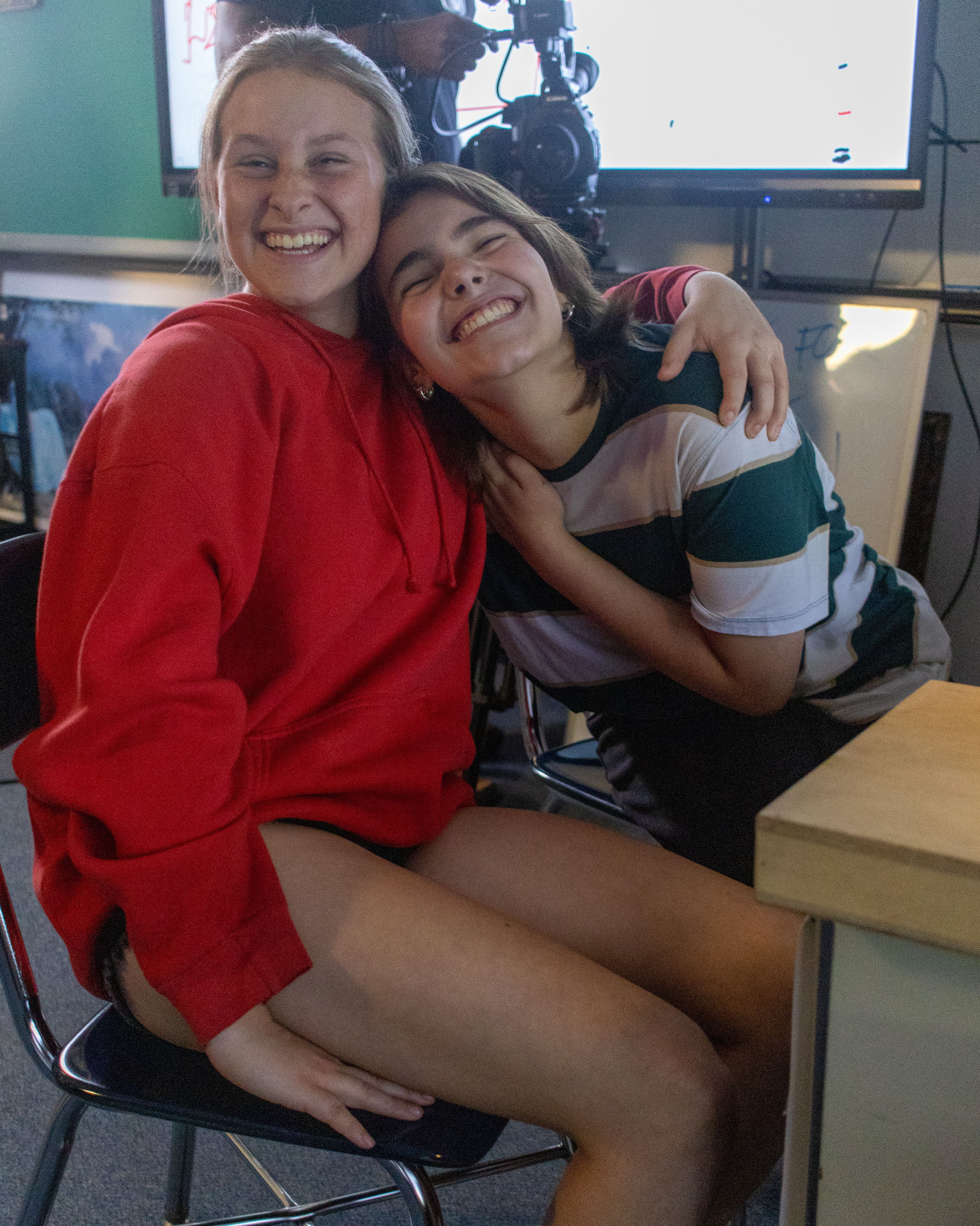 Two students laugh together on set in front of the camera and monitor