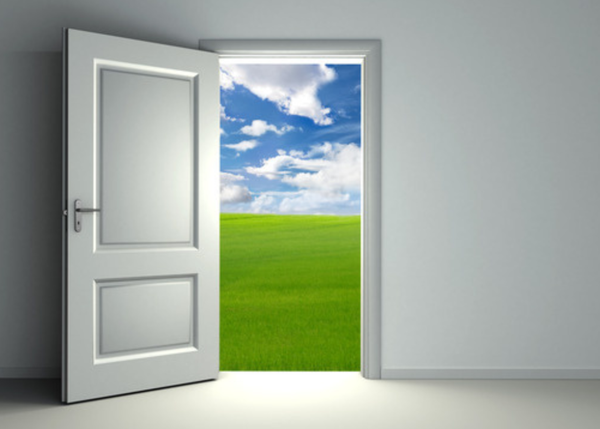 an open door leading to a clear sky and green pasture