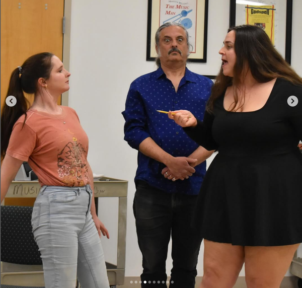 Me, as Merriman, standing between two women, one of whom is threatening the other with a pointed pencil. I'm standing with my hands folded in front of me, wide-eyed, trying to be invisible.